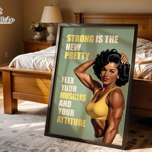 May include: A framed wall art print featuring a muscular person with dark curly hair wearing a yellow sports bra. The sage green background displays the text: STRONG IS THE NEW PRETTY, FLEX YOUR MUSCLES AND YOUR ATTITUDE in bold yellow letters.