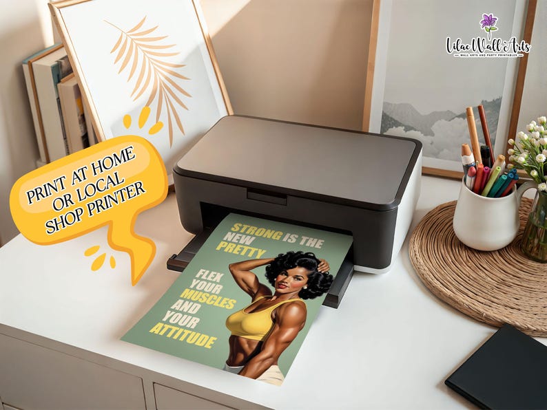May include: A black and grey desktop printer outputting a printed sheet featuring a muscular individual in a yellow top. The text on the print reads: STRONG IS THE NEW PRETTY, FLEX YOUR MUSCLES AND YOUR ATTITUDE. A yellow speech bubble graphic says PRINT AT HOME OR LOCAL SHOP PRINTER.