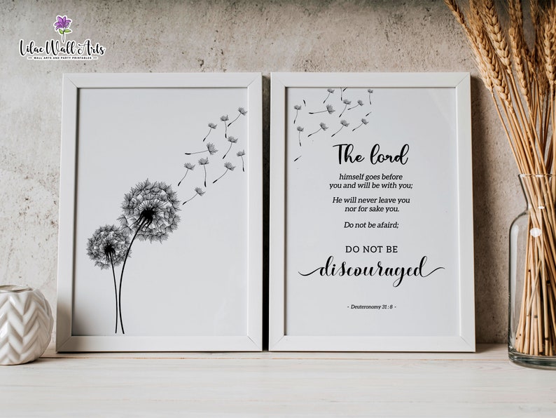 May include: Two black and white prints in white frames. The left print features two dandelion seeds with seeds blowing in the wind. The right print features a bible verse from Deuteronomy 31:8, "The Lord himself goes before you and will be with you: He will never leave you nor forsake you. Do not be afraid; do not be discouraged."