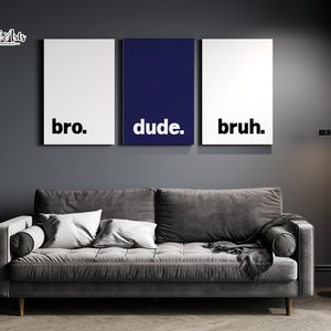 May include: Three framed prints with the words "bro", "dude", and "bruh" in black text on a white background. The middle print is navy blue. The prints are hanging on a dark gray wall above a gray couch.