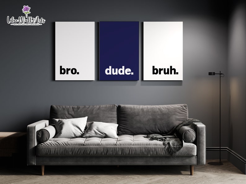 May include: Three framed prints with the words "bro", "dude", and "bruh" in black text on a white background. The middle print is navy blue. The prints are hanging on a dark gray wall above a gray couch.