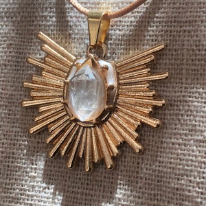 May include: A gold pendant necklace featuring a clear quartz crystal at its centre. The pendant is shaped like a sun with numerous rays.
