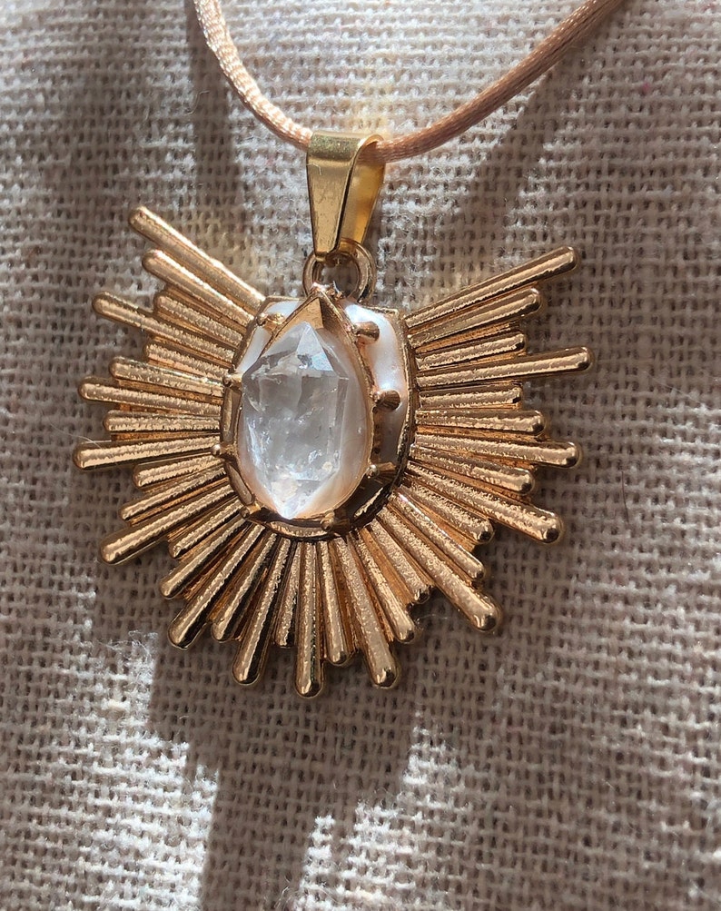 May include: A gold pendant necklace featuring a clear quartz crystal at its centre. The pendant is shaped like a sun with numerous rays.