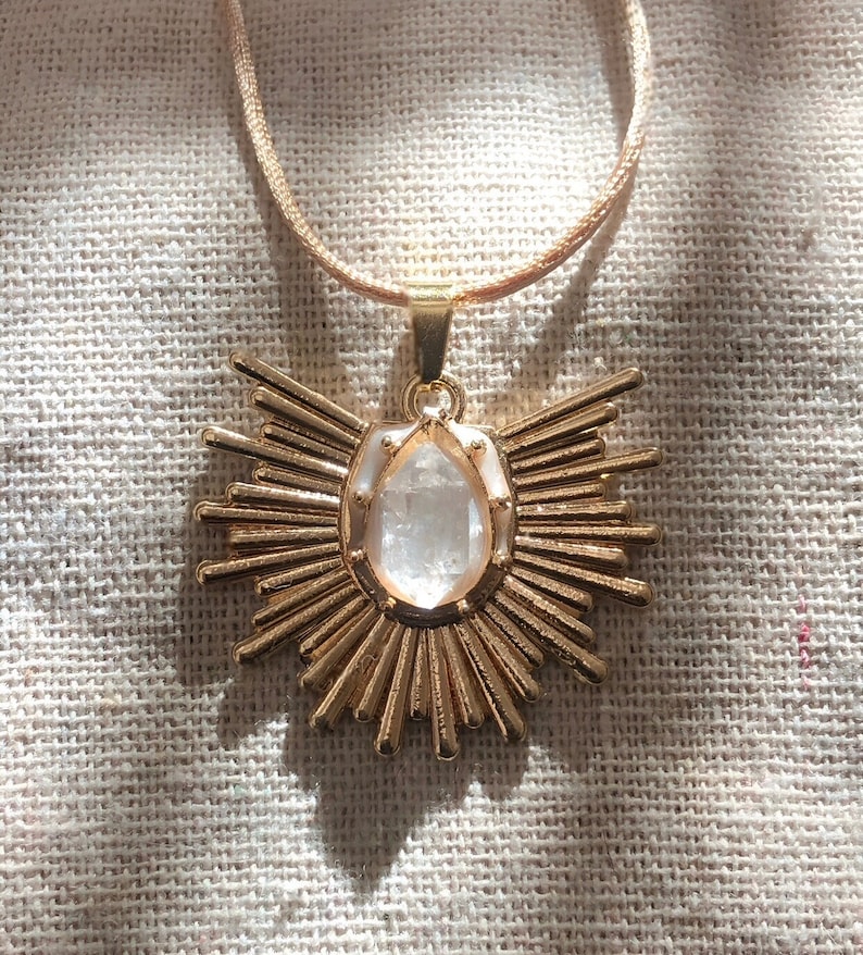 May include: A gold necklace featuring a large, clear crystal pendant in the shape of a sunburst.