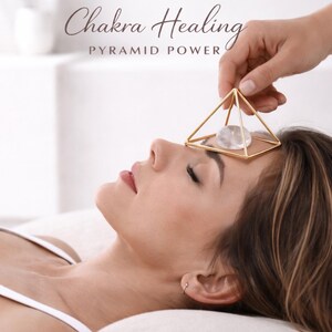 Puede incluir: Una estructura piramidal de metal dorado que contiene una piedra de cristal transparente, lisa y de forma ovalada. El texto "Chakra Healing" y "PYRAMID POWER" est&aacute; impreso en letras marr&oacute;n oscuro sobre la pir&aacute;mide.
