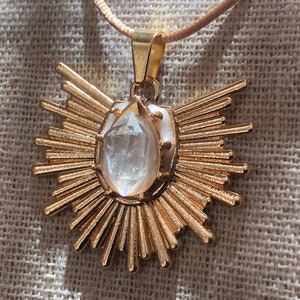 May include: A gold pendant necklace featuring a clear quartz crystal at its centre. The pendant is shaped like a sun with numerous rays.