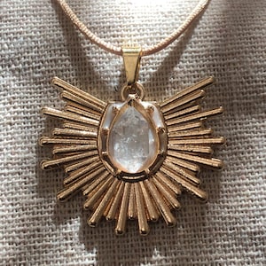 May include: A gold necklace with a clear crystal pendant in the shape of a sunburst.