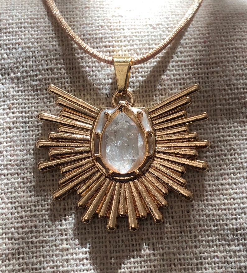 May include: A gold necklace with a clear crystal pendant in the shape of a sunburst.