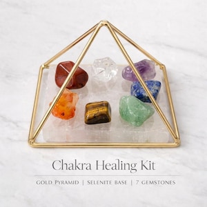 Puede incluir: Un kit de sanaci&oacute;n de chakras con una estructura piramidal de metal dorado, una base cuadrada de selenita y siete piedras preciosas variadas en rojo, naranja, amarillo-marr&oacute;n, transparente, verde, azul y morado. Texto: Chakra Healing Kit.