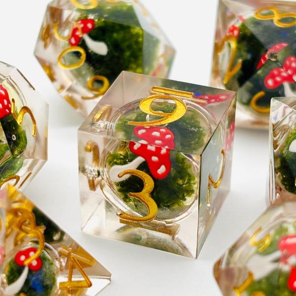 May include: Set of six clear resin dice with gold numbers and a mushroom and moss design. Each die has a different number from 1 to 6.