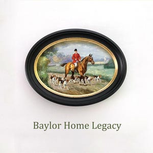 May include: An oval framed oil painting depicting a man on horseback riding through a field with a pack of hounds. The man is wearing a red coat and a black hat. The horse is brown and white. The hounds are black and white. The painting is set against a backdrop of green trees and a blue sky. The frame is black with gold accents. The text "Baylor Home Legacy" is printed below the painting.