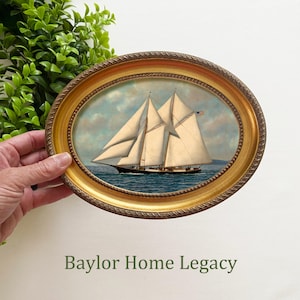 May include: A framed oval painting of a sailboat with white sails and a blue hull, set against a blue sky with white clouds. The frame is gold with a rope-like design.