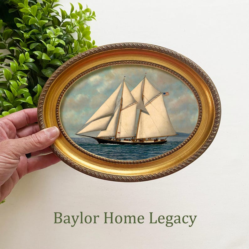 May include: A framed oval painting of a sailboat with white sails and a blue hull, set against a blue sky with white clouds. The frame is gold with a rope-like design.