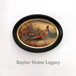 May include: A black oval frame with gold trim surrounds a painting of a pheasant in a forest setting. The pheasant is brown, orange, and black with a long tail. The painting is titled "Baylor Home Legacy".