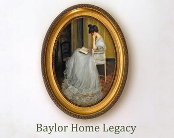May include: A framed oil painting of a woman in a white dress sitting in a chair and reading a book. The painting is in an oval gold frame with a decorative border. The text "Baylor Home Legacy" is below the painting.