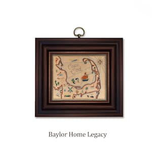 May include: Framed artwork featuring a map of Cape Cod, with embroidered details in shades of beige, red, and blue. The artwork is encased in a dark brown wooden frame with a brass hanging ring. The text "Cape Cod" is visible.