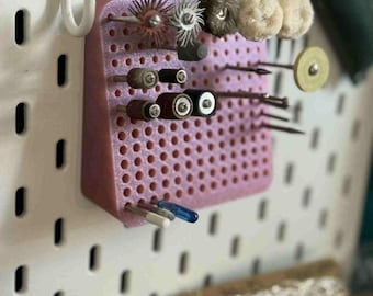 May include: A pink pegboard organizer with various small tools and accessories. The organizer is mounted on a white pegboard and holds items like grinding bits, polishing wheels, and other craft or jewelry-making tools.