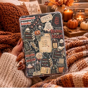 May include: A clear protective case for an e-reader featuring a collage of dark, autumn-themed stickers including skulls, pumpkins, black cats, stacks of books, and text such as Emotional Support Kindle and Reading Is My Escape.
