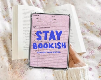 Puede incluir: Una funda transparente para tableta con un fondo rosa que presenta las palabras "STAY BOOKISH" en azul. La tableta se sostiene frente a un libro abierto. También se ve el texto "READ PAST YOUR BEDTIME".