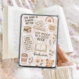 May include: A clear tablet case with a book-themed design, featuring text like "The Book Is Always Better" and "Lose Myself In A Good Book." The case has illustrations of books, flowers, a rainbow, and a teddy bear. An open book is in the background.