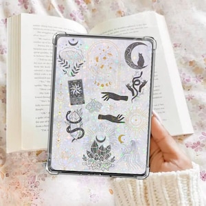 Könnte beinhalten: Eine transparente Handyhülle mit glitzerndem Hintergrund und schwarz-weißen Illustrationen von Monden, Sternen, Kristallen, Händen, einer Katze und einer Schlange. Die Hülle hat einen holografischen Effekt.