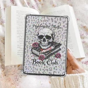 May include: A clear phone case with a silver leopard print design. The case features a skull, books, and roses with the words "Psychological Thriller Book Club". The case is held in front of an open book.