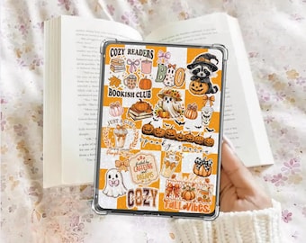 Könnte beinhalten: Eine transparente Handyhülle mit einem herbstlichen Design mit Kürbissen, Geistern und dem Text "Cozy Readers" und "Bookish Club". Die Hülle hat einen karierten orange-weißen Hintergrund und wird über einem offenen Buch gehalten.