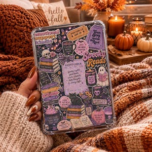May include: A clear protective tablet case featuring a collage of stickers with Halloween and reading themes. The stickers include text like emotional support kindle, spooky reads, and guest check, alongside illustrations of skulls, pumpkins, and cats.