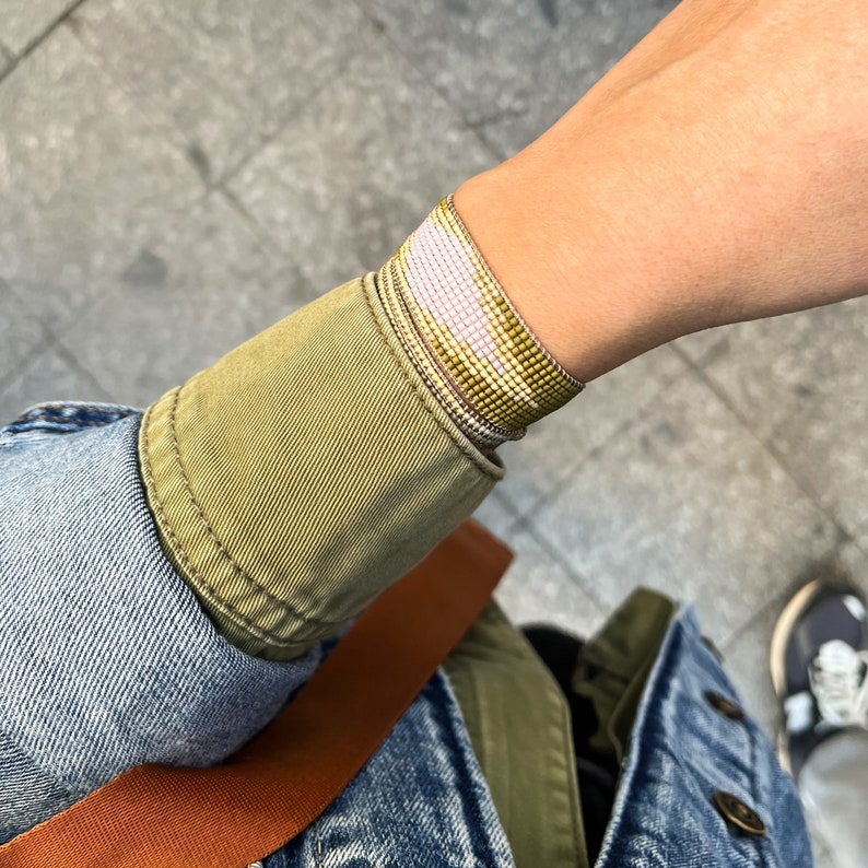 May include: A close-up of a person's wrist wearing a layered beaded bracelet with white, pink, and gold beads.
