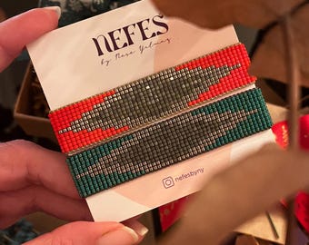 May include: Two beaded bracelets, one red and one green, with silver accents. The bracelets are displayed on a white card with the text "NEFES by Nese Yilmaz" and the Instagram handle "@nefesbyny".