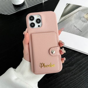 Op de afbeelding: Een roze leren telefoonhoesje met een ingebouwd portemonnee en een gouden inscriptie die "Phoebe" luidt.