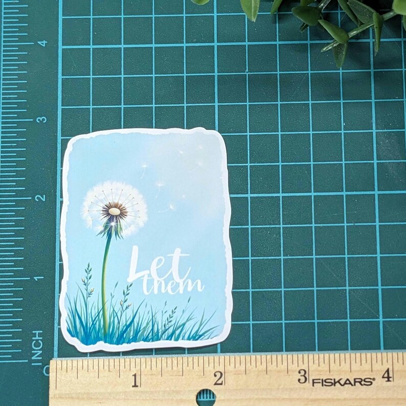 May include: A white dandelion with seeds blowing in the wind against a blue sky background. The text "Let them" is written in white cursive lettering.