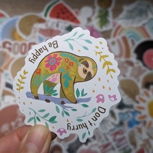May include: A white sticker with a colorful sloth on a branch. The sloth is decorated with floral patterns and the text "Be happy, Don't hurry" is written around it.
