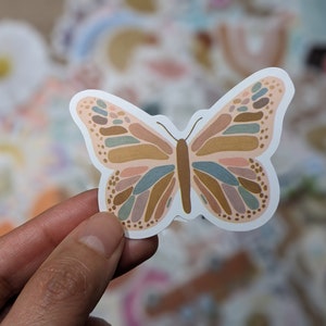 May include: A sticker of a butterfly with a pink, brown, and blue abstract pattern. The butterfly is outlined in white.
