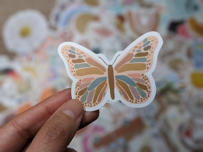 May include: A sticker of a butterfly with a pink, brown, and blue abstract pattern. The butterfly is outlined in white.