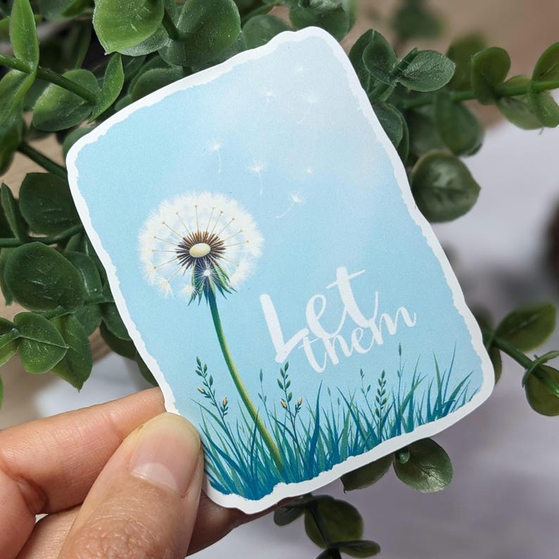 May include: A blue and white sticker with a dandelion and the text "Let them" in white. The dandelion is blowing seeds in the wind.