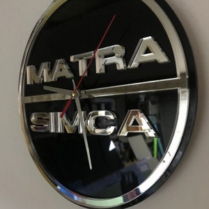 Può includere: Un orologio nero e argento con le parole "MATRA SIMCA" in lettere argentate sul quadrante.