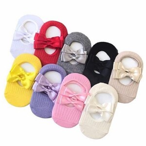 K&ouml;nnte beinhalten: Eine Auswahl an F&uuml;&szlig;lingen in verschiedenen Farben, jeweils mit einer Satinschleife verziert. Farben sind Wei&szlig;, Rot, Grau, Schwarz, Gelb, Lila, Rosa und Beige. Die Socken sind f&uuml;r das Tragen mit Schuhen konzipiert und aus weichem Material gefertigt.
