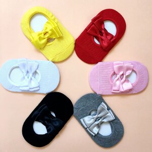 K&ouml;nnte beinhalten: Sechs Paar F&uuml;&szlig;linge in verschiedenen Farben: Gelb, Rot, Hellblau, Rosa, Schwarz und Grau. Jede Socke hat eine Satinschleife in einer passenden oder komplement&auml;ren Farbe. Die Socken sind f&uuml;r das Tragen mit Ballerinas oder anderen Schuhen mit niedrigem Schnitt konzipiert.