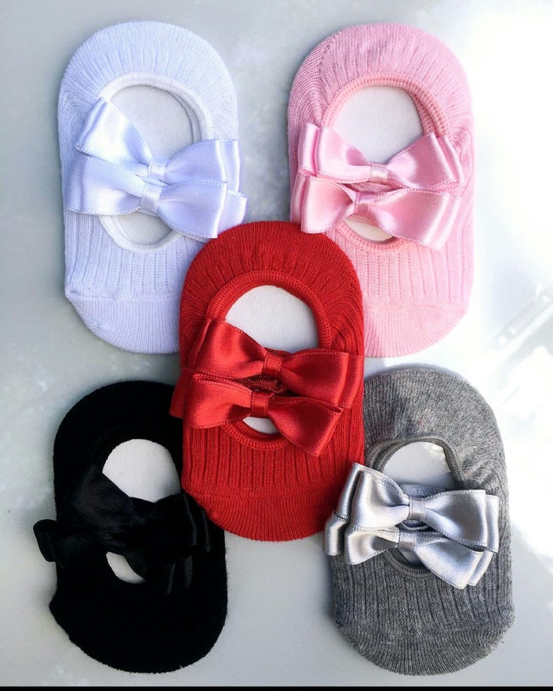 K&ouml;nnte beinhalten: F&uuml;nf Paar F&uuml;&szlig;linge in verschiedenen Farben: Wei&szlig;, Rosa, Rot, Schwarz und Grau. Jede Socke hat eine gro&szlig;e Satinschleife in einer passenden oder komplement&auml;ren Farbe. Die Socken sind gerippt und f&uuml;r das Tragen mit Schuhen konzipiert.