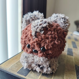 May include: A small brown and gray plush toy with black eyes. The toy is made of a soft, fuzzy material and has a rounded shape.