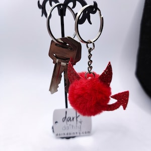 May include: Red fuzzy keychain with devil horns and glitter. The keychain is attached to a silver chain and a silver key ring.