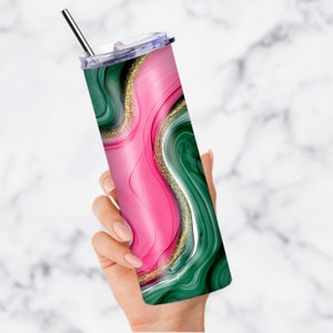 May include: A stainless steel tumbler with a green and pink marble design and gold glitter accents. The tumbler has a clear lid and a straw.