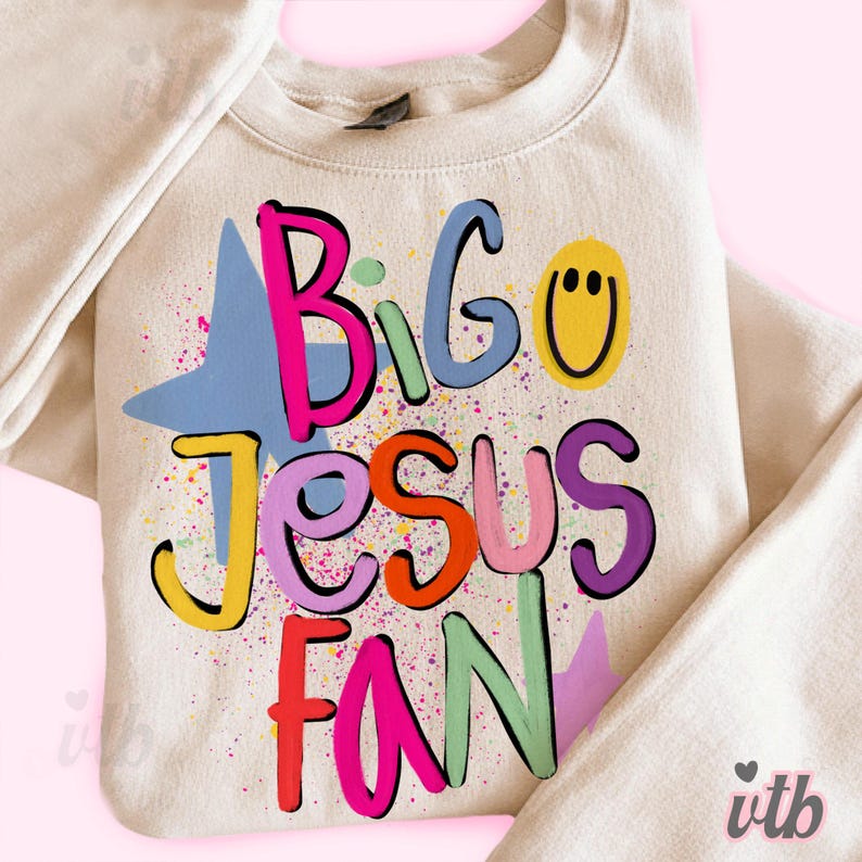 以下が含まれることがあります： クリーム色のスウェットシャツ。カラフルで遊び心のあるフォントで「Big Jesus Fan」と書かれています。デザインには青い星、黄色のスマイリーフェイス、カラフルなペイントスプラッターが含まれています。スウェットシャツはクルーネックと長袖です。