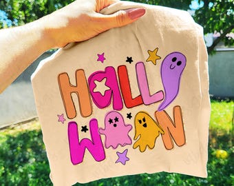 May include: A beige t-shirt featuring the word "HALLOWEEN" in orange, pink, and purple. The design includes cartoon ghosts and stars. The text "utbdesigns" is in the bottom right corner.