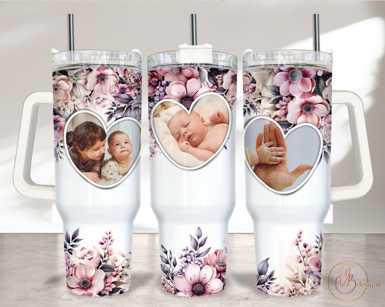 May include: Three white stainless steel tumblers with floral designs and heart-shaped photo frames. The tumblers have lids and straws. The photo frames contain images of a baby, two children, and a hand holding a baby's hand.