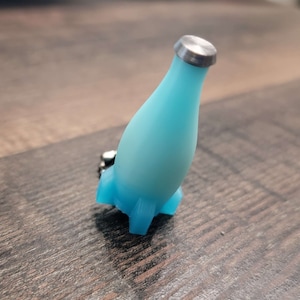 May include: A light blue bottle shaped keychain with a silver top. The bottle has a rounded bottom and a small, flat base.