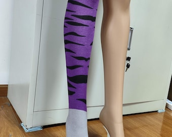 May include: Purple and black tiger stripe knee-high socks with a gray foot featuring purple paw prints. The socks are displayed on a mannequin leg. The other leg is a nude color.