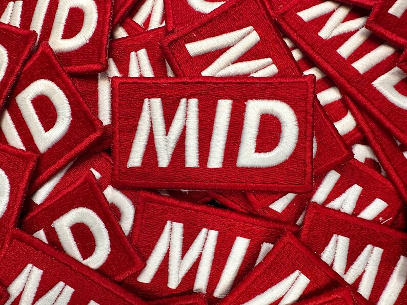 May include: A collection of red rectangular patches with the word "MID" embroidered in white. The patches are densely packed together, creating a textured surface. The white lettering stands out against the vibrant red background.