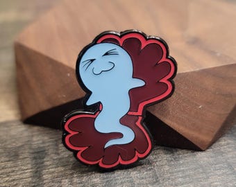 May include: A blue ghost enamel pin with a smiling face, set against a dark red, scalloped background with a black outline. The pin is a whimsical accessory.